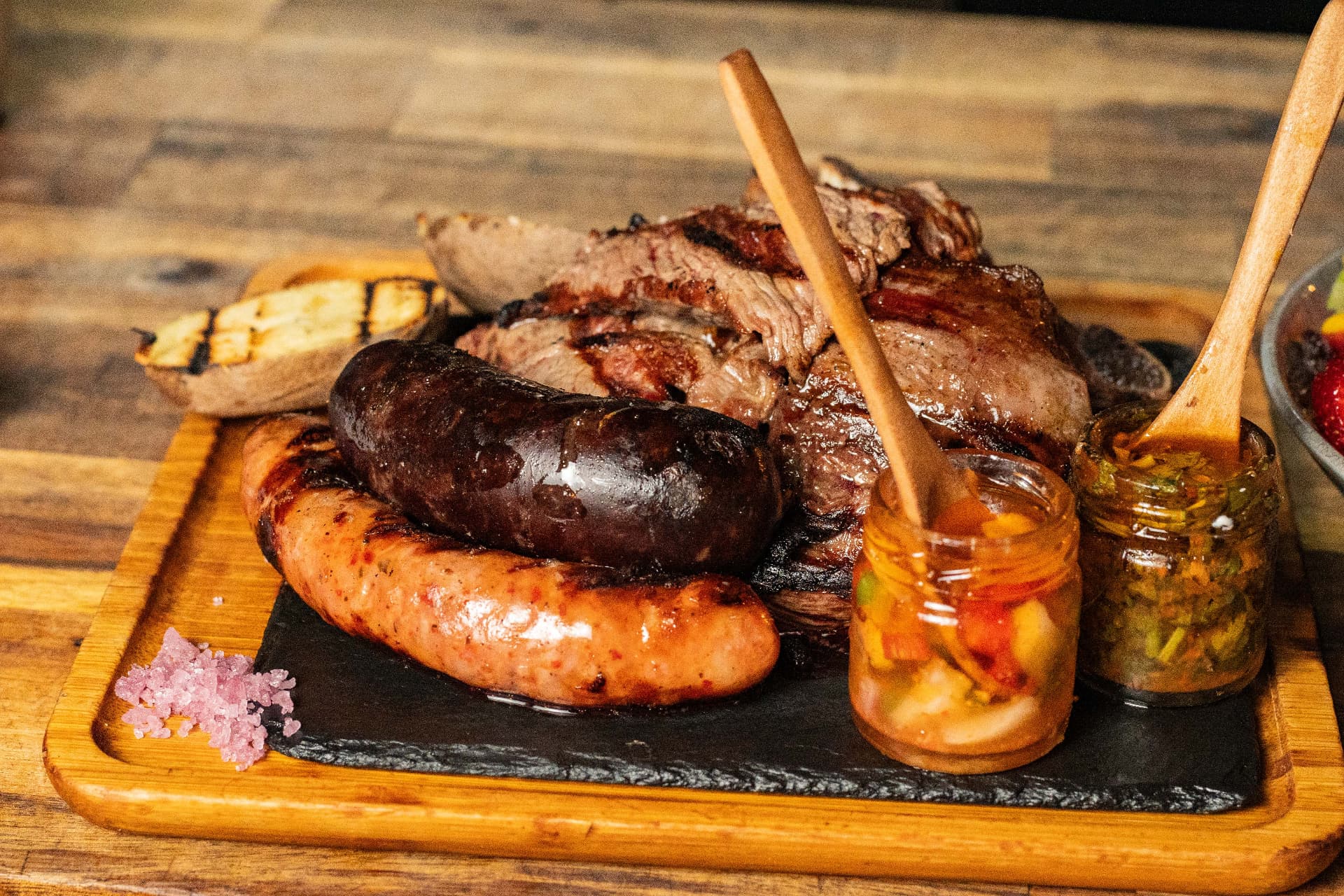 Parrillada de carnes y embutidos con salsas sobre una tabla de madera